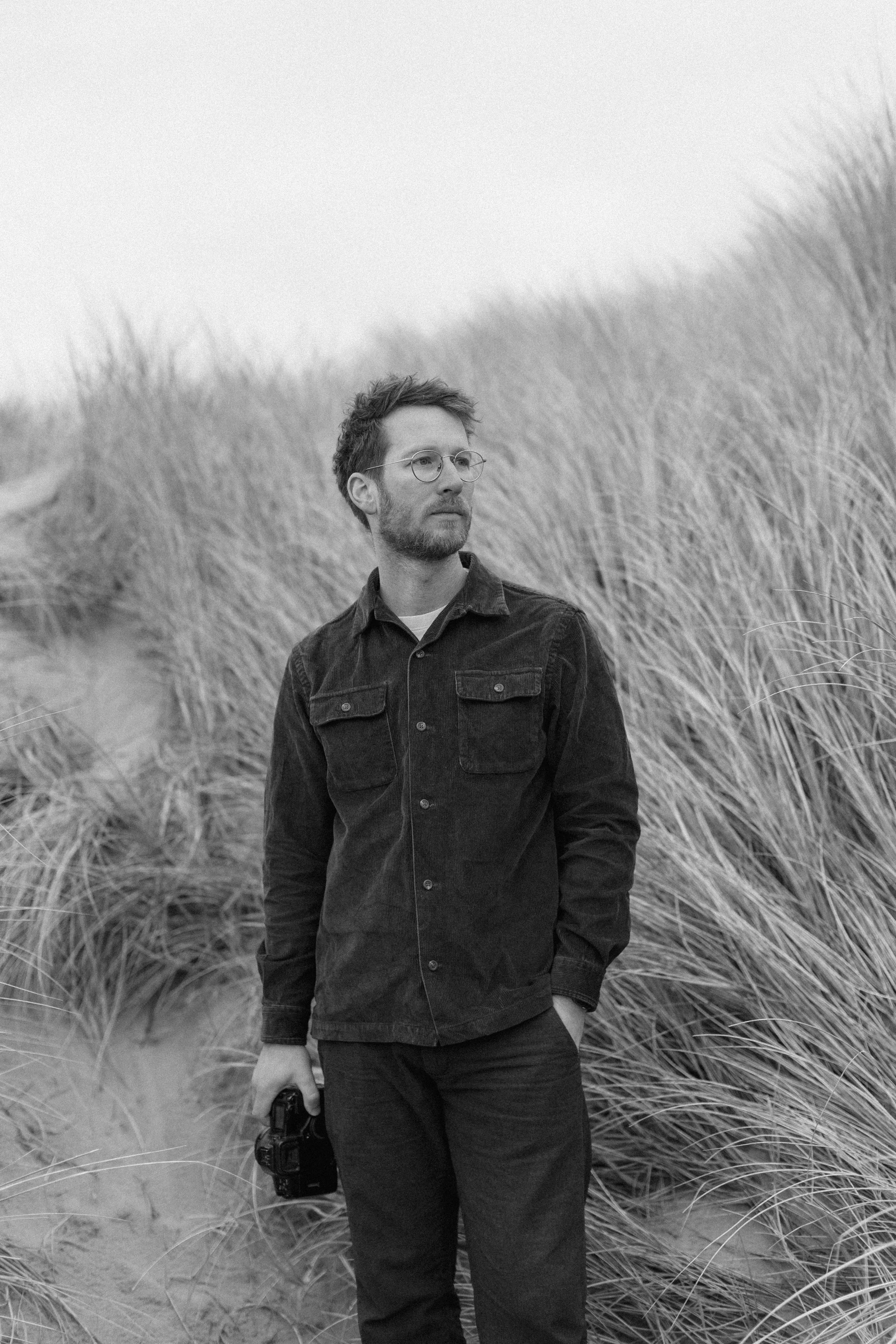 Christoph standing in the dunes, camera in one hand, looking off to the side