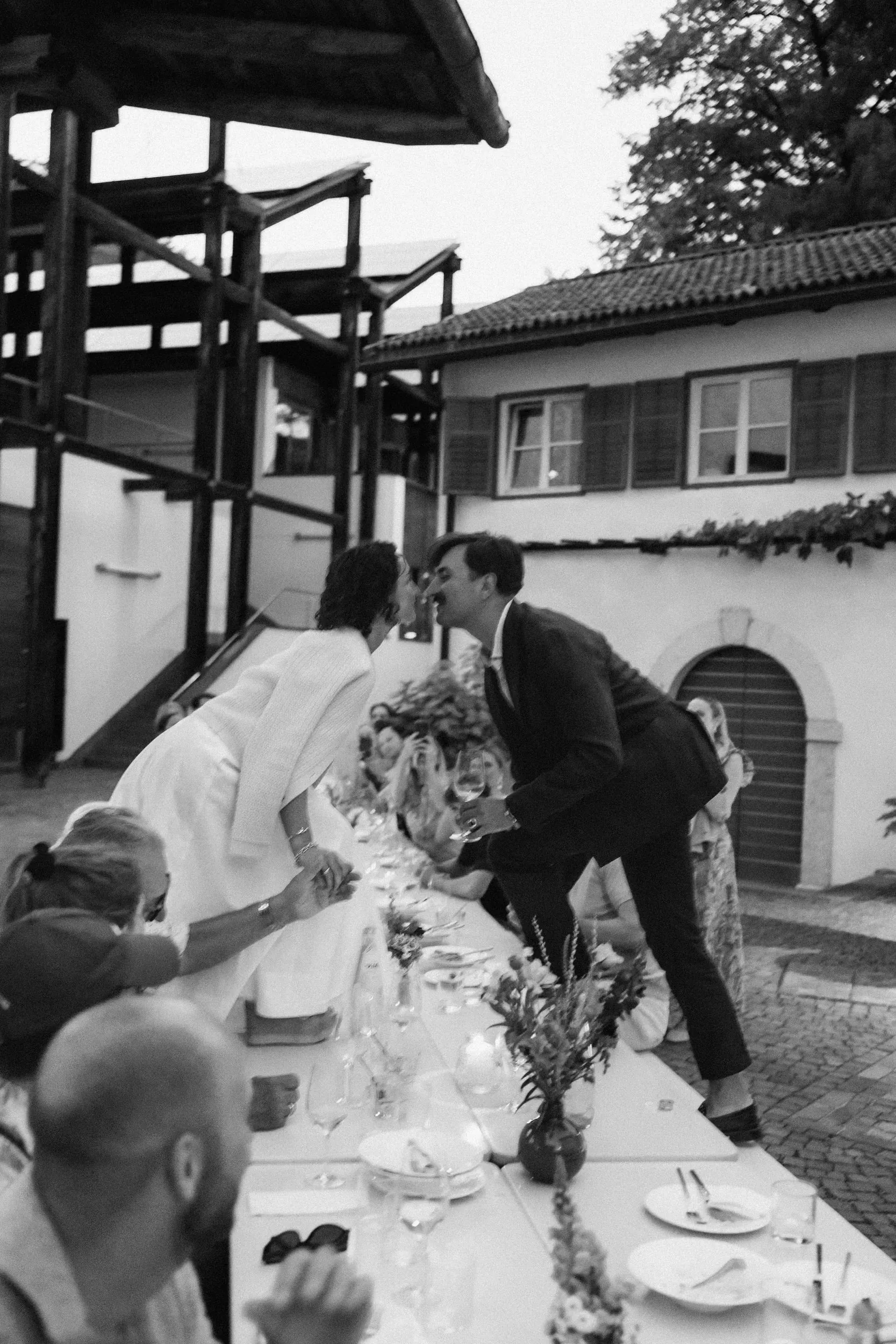 Guests leaning across the long table, the couple kissing at the far end