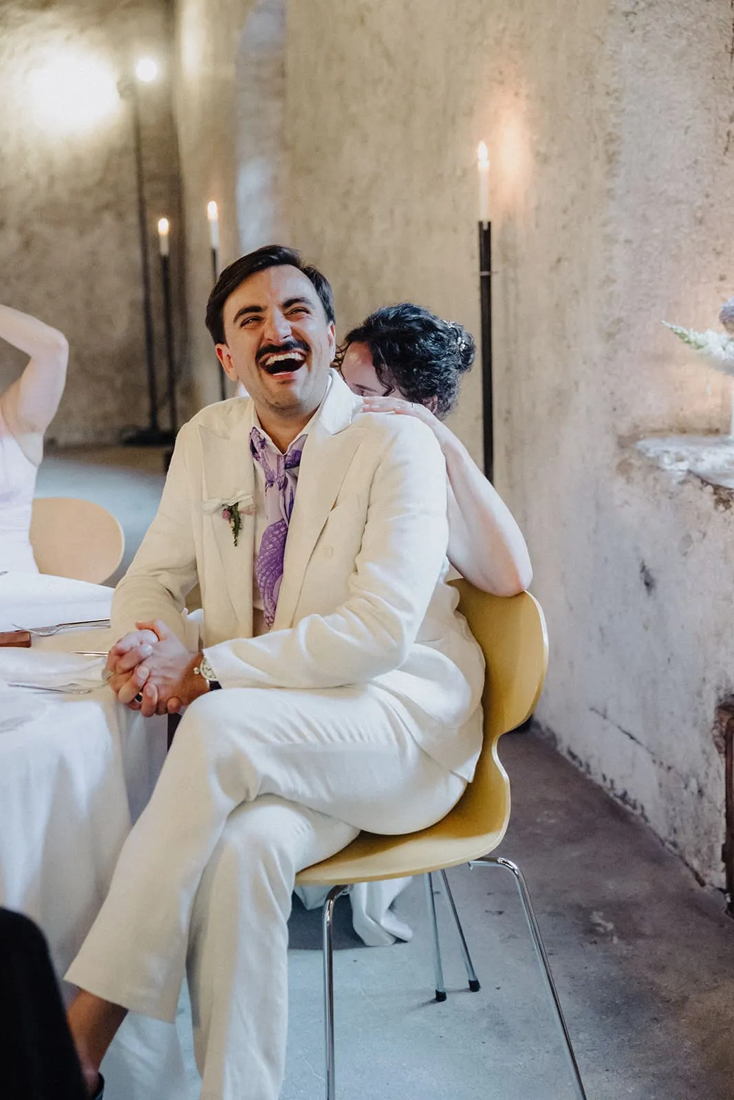 The groom laughing on his chair, the bride leaning on his shoulder