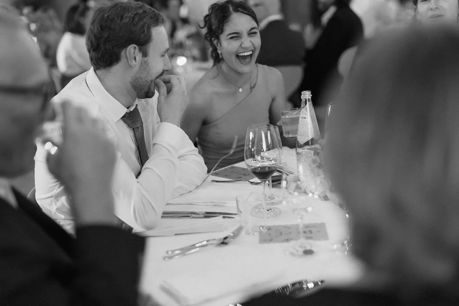 Two guests laughing at the dinner table over a glass of red wine