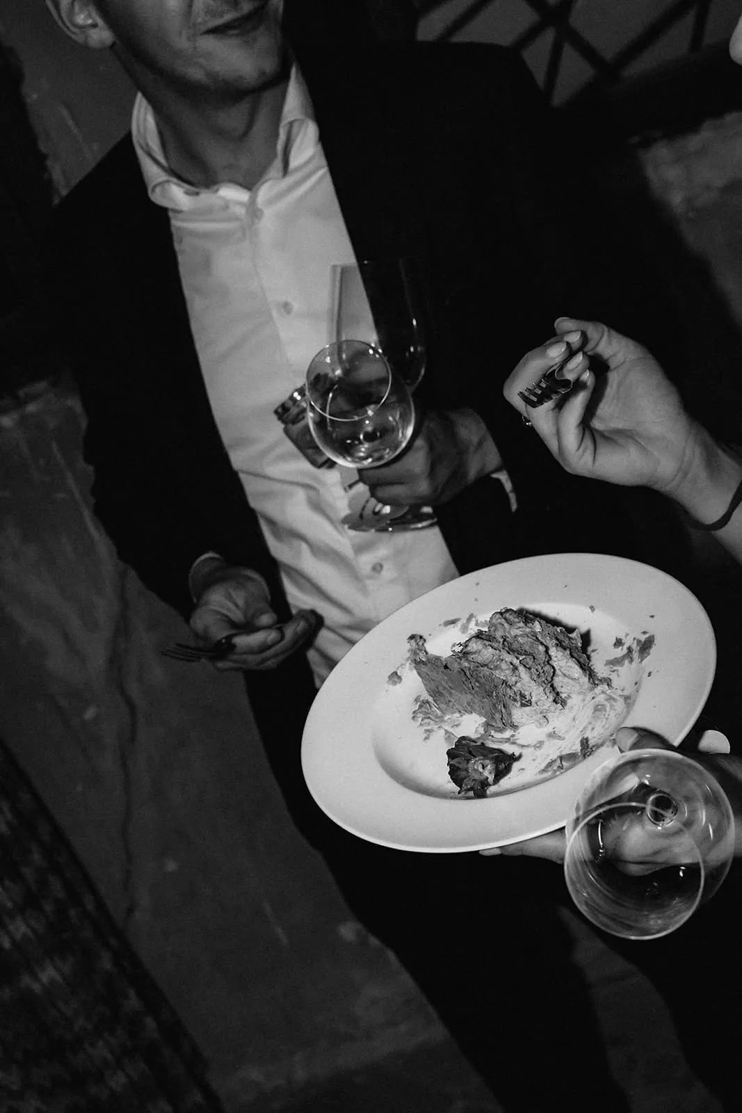A guest with a plate of cake and a glass of wine in the dark