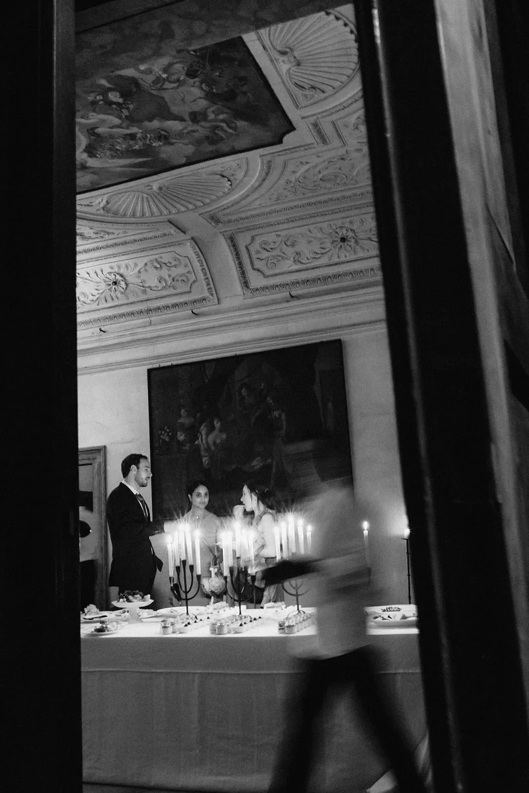 The candlelit dessert table under the painted ceiling, someone walking past