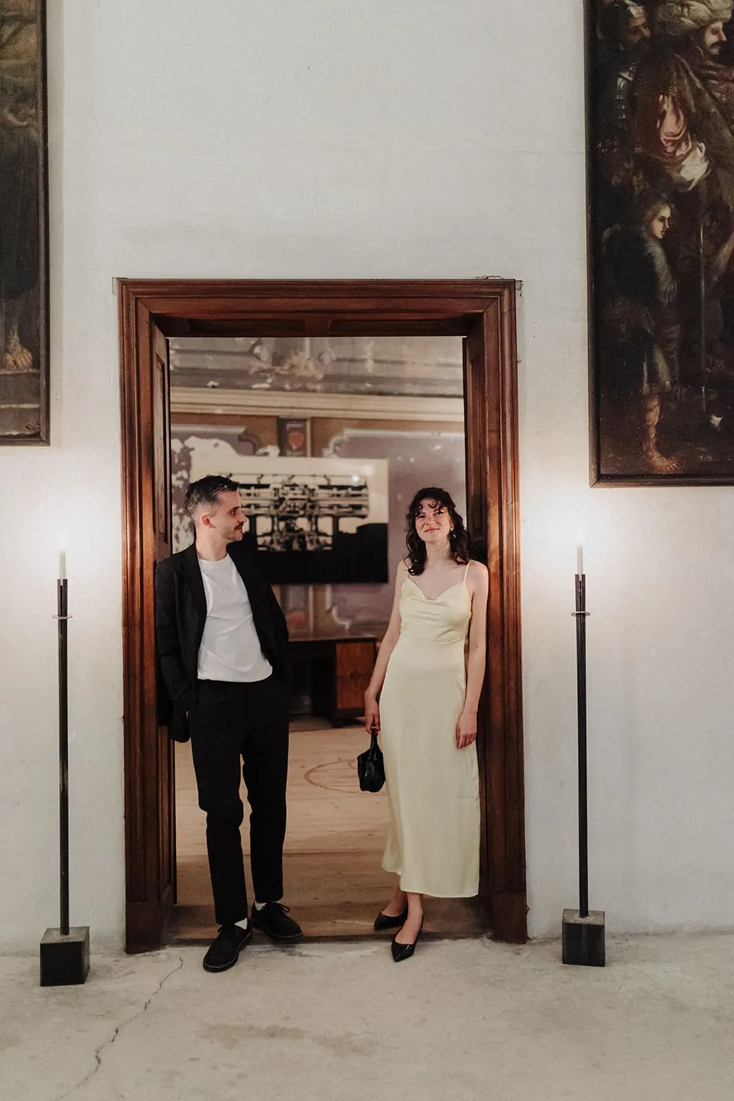 Two guests standing in a lit doorway between the paintings