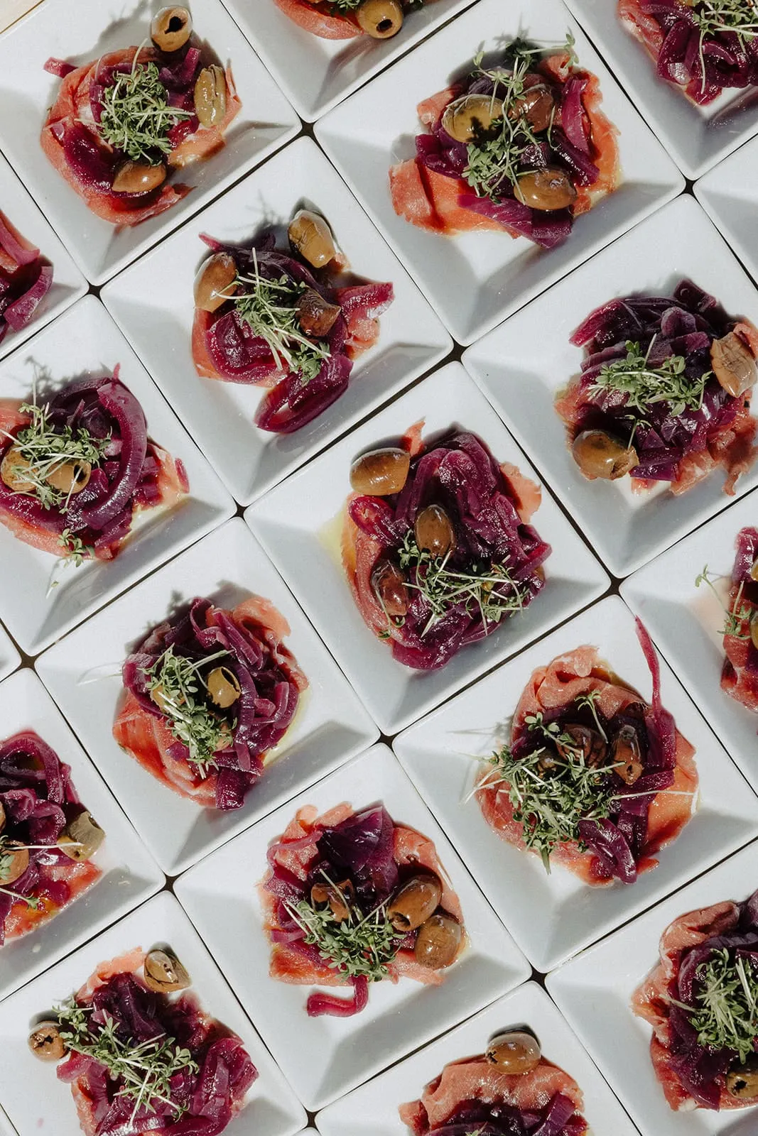 Rows of small square plates with ham and red onion, seen from above