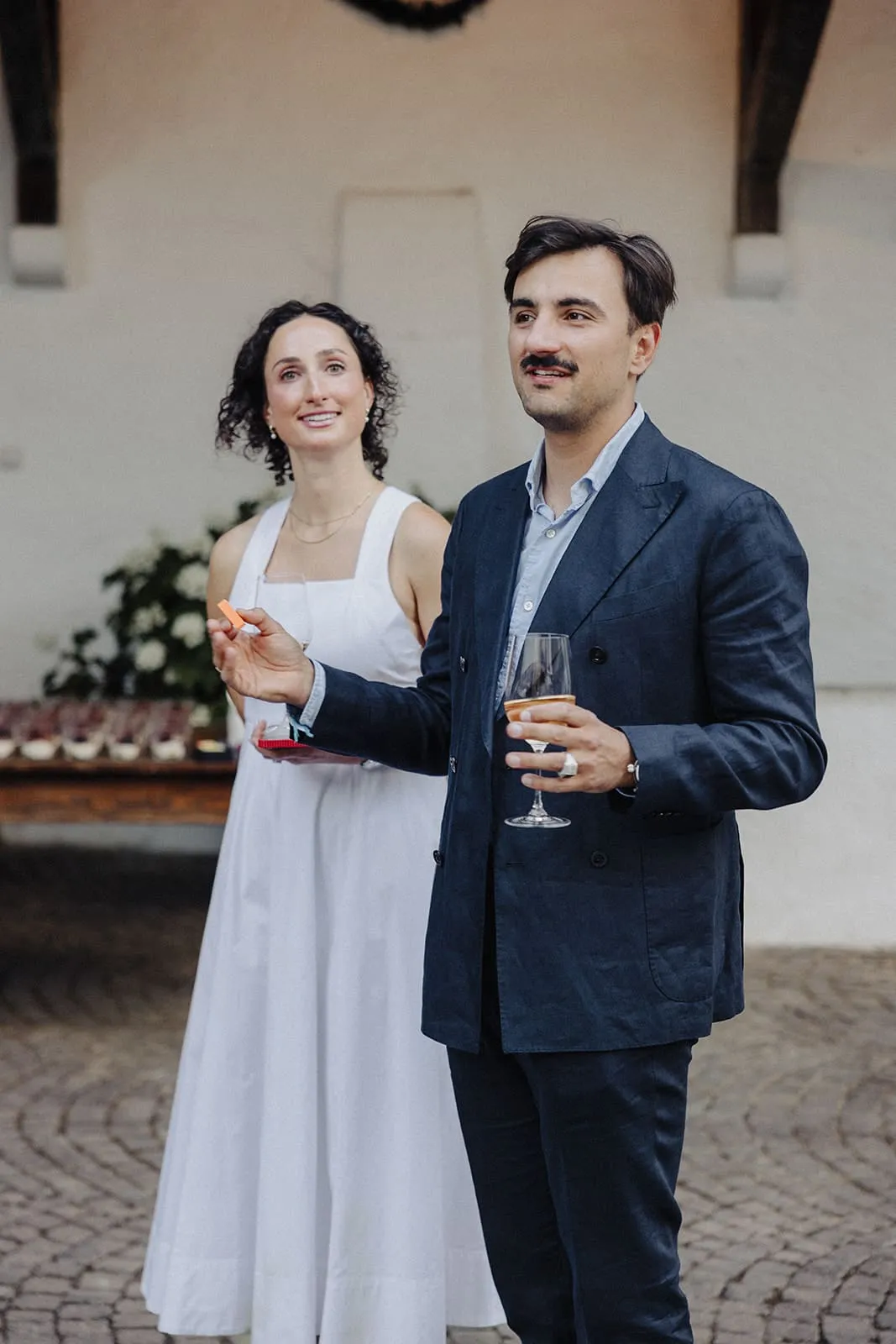 The couple standing in the courtyard with a drink and a canape