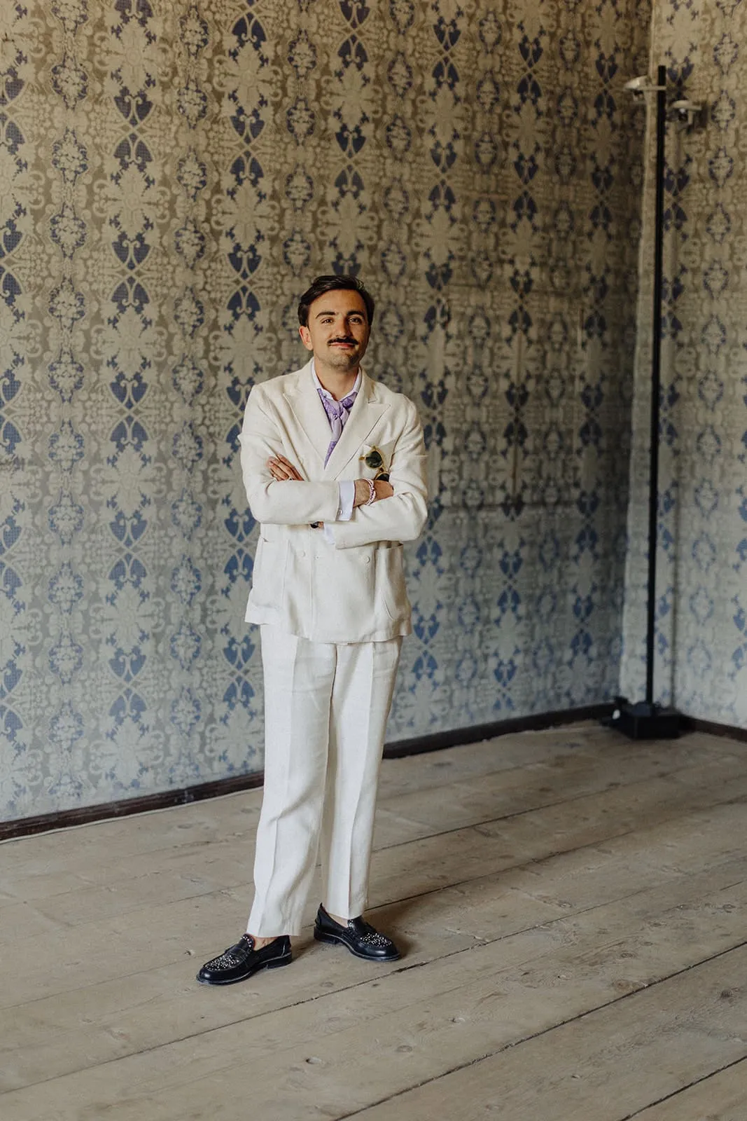 The groom alone in the papered room, arms crossed, waiting
