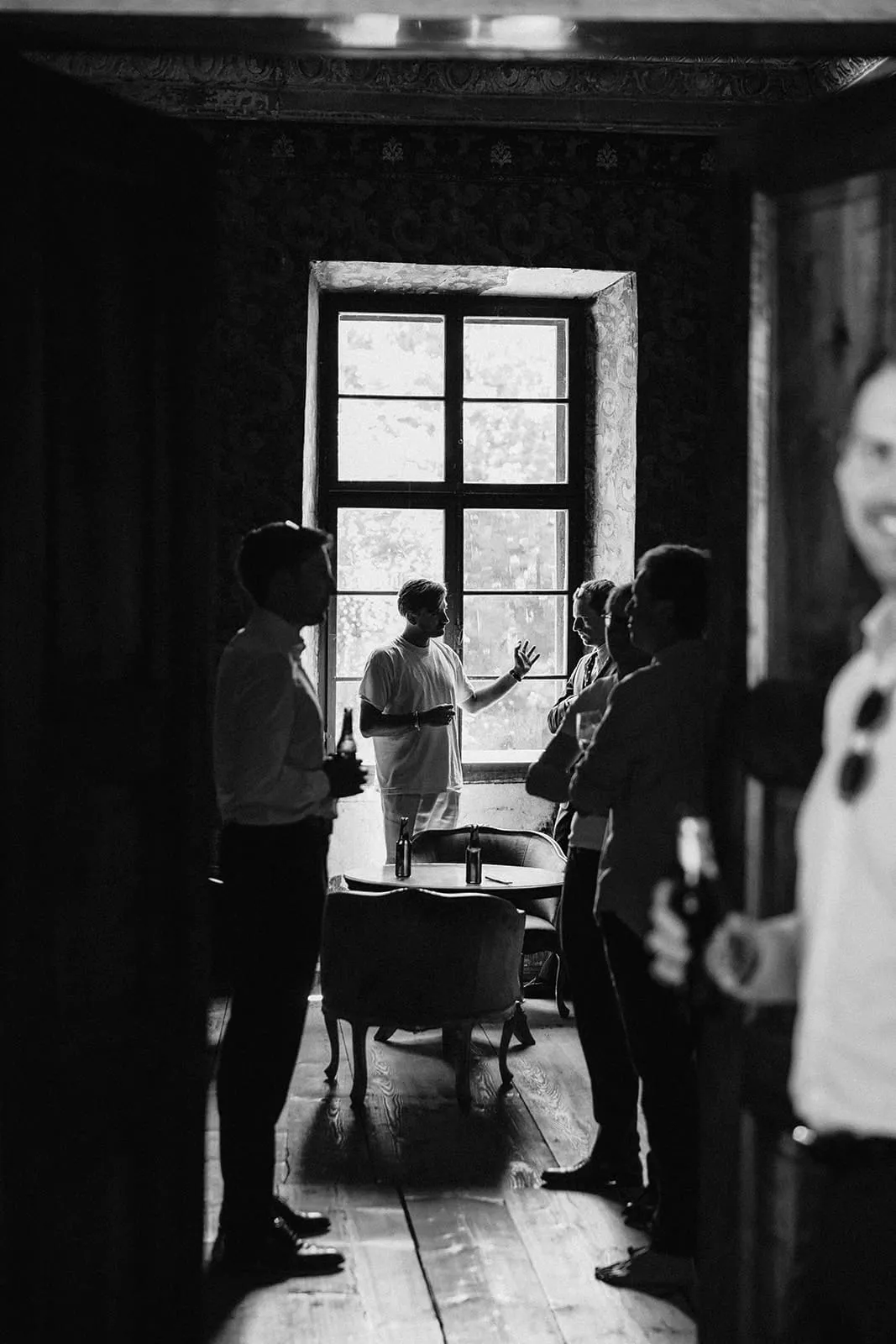 The groom and his friends at the window in a dark room, beers in hand