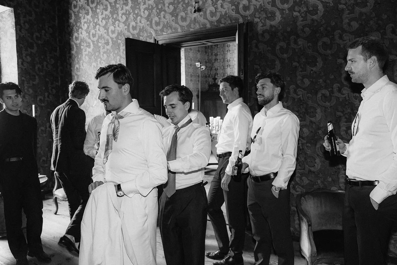 The groom and his friends half dressed in the papered room, beers in hand
