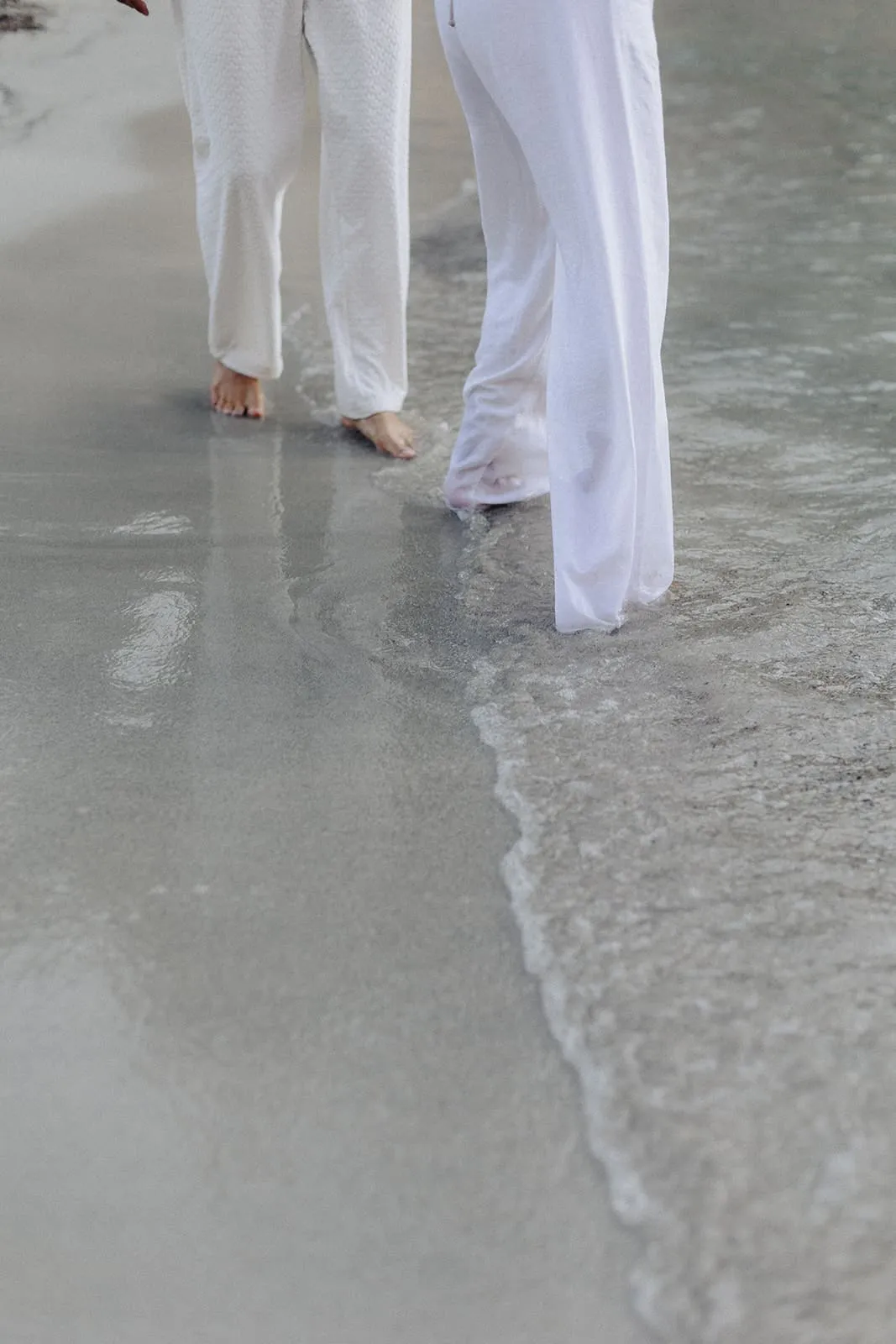 Two pairs of bare feet at the waterline as a wave runs in