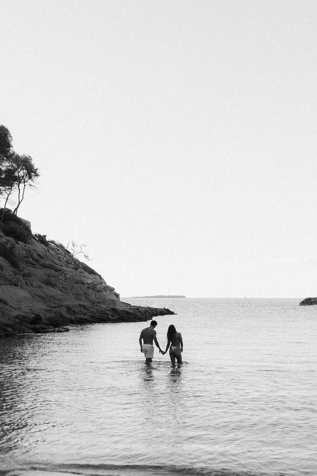 The couple wading into the sea hand in hand, seen from the shore