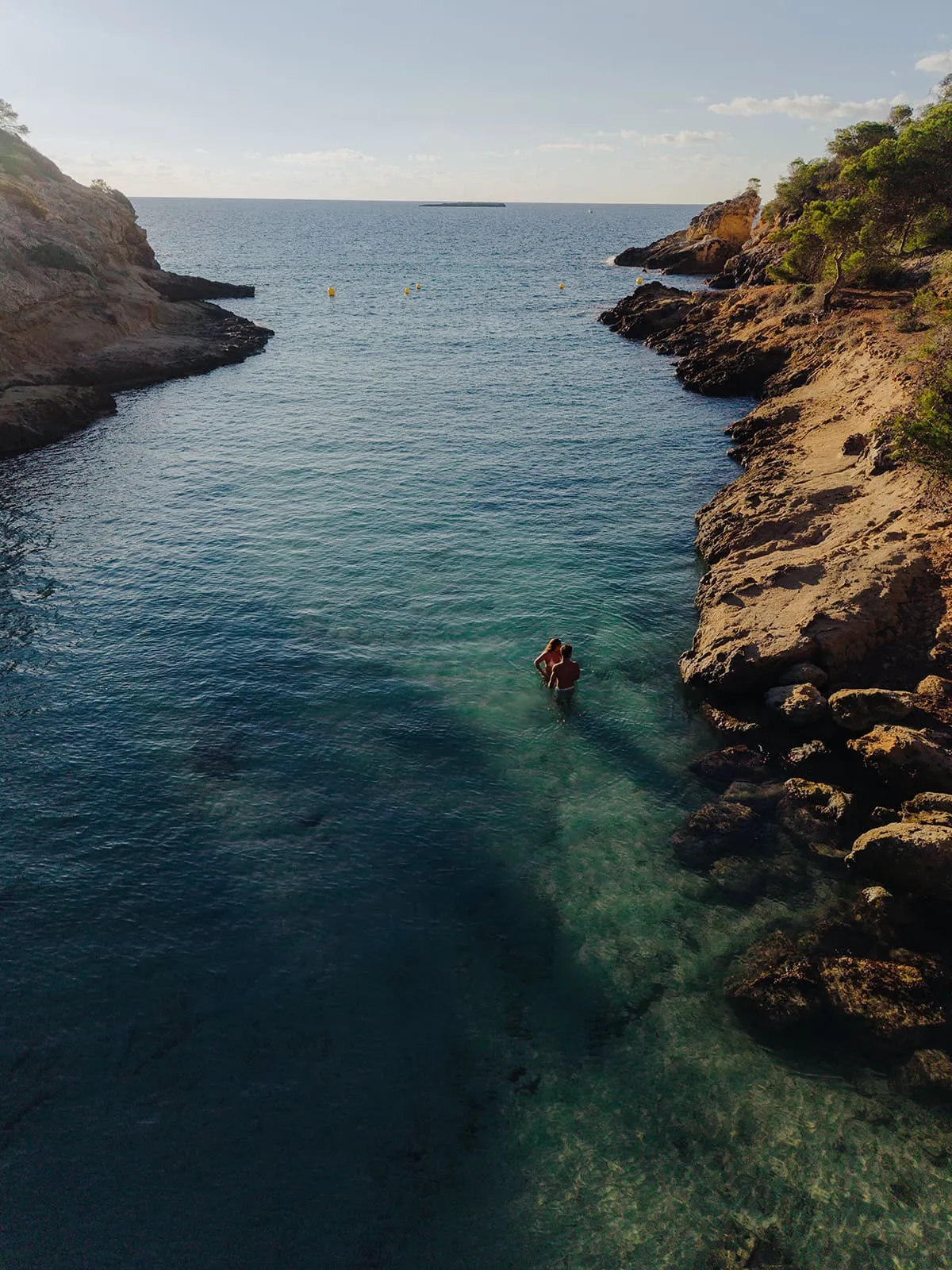 The couple standing alone in a turquoise cove, seen from above