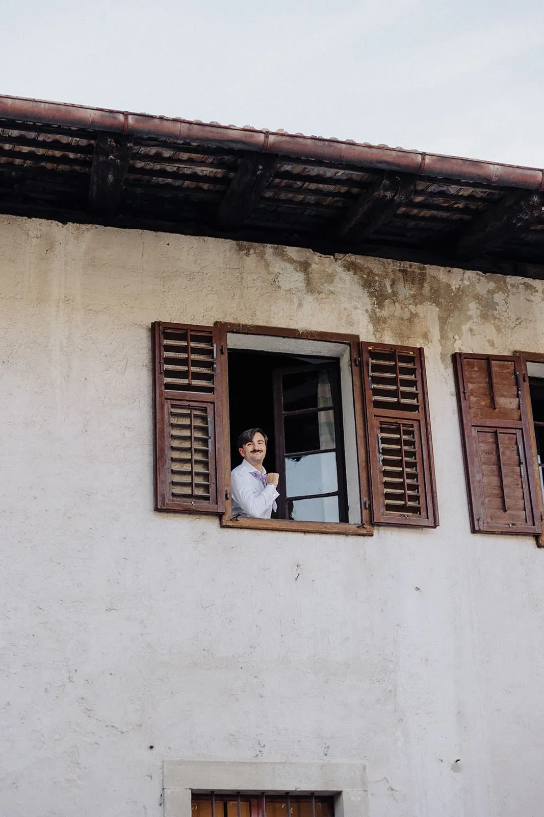 The groom leaning out of a shuttered window above the courtyard