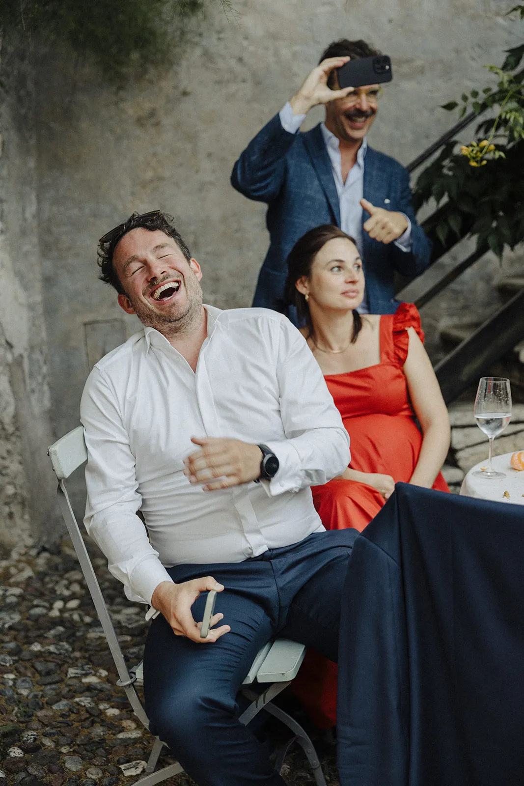 Guests laughing on garden chairs, one holding up a phone