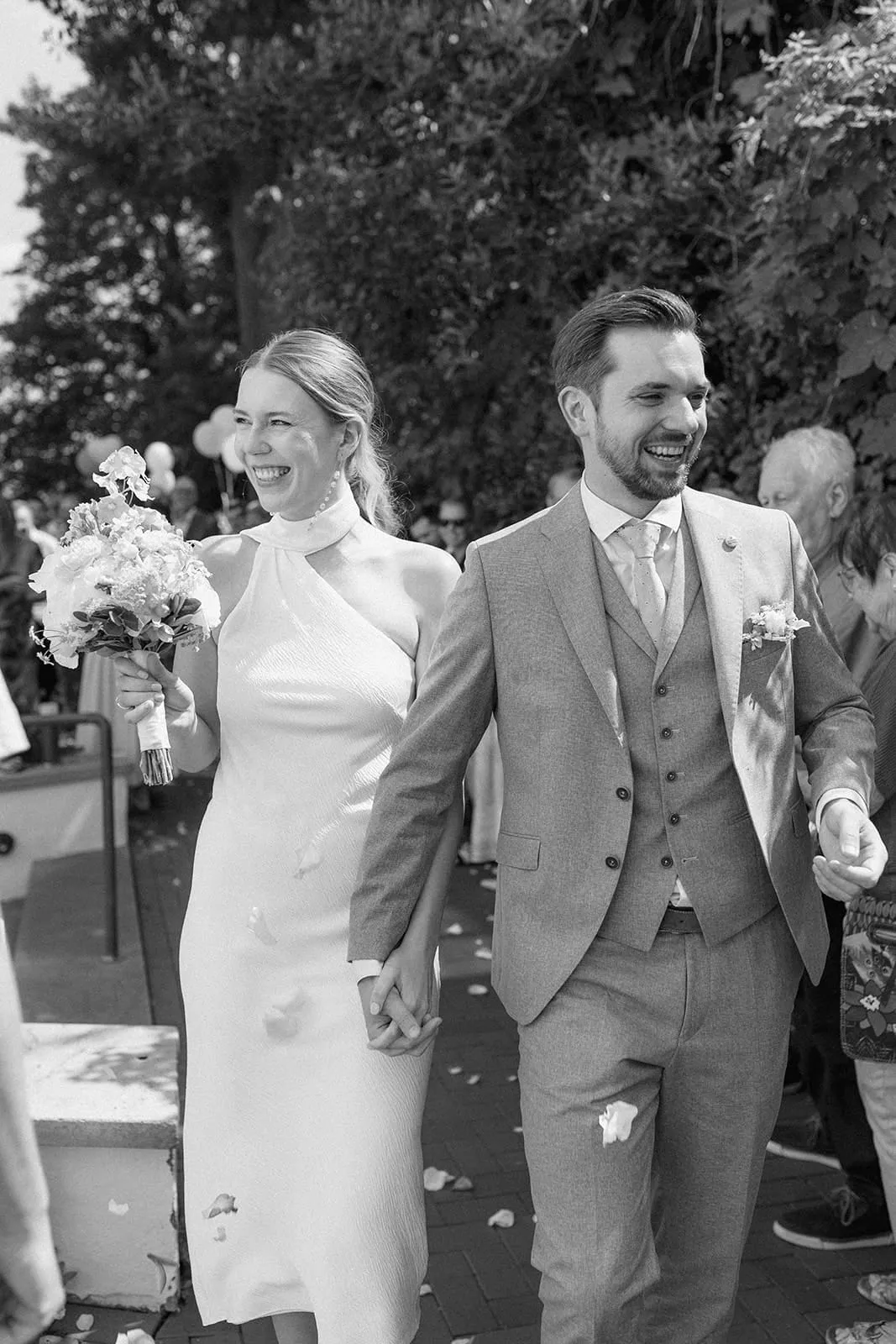 The couple walking out through confetti, both laughing, guests behind them