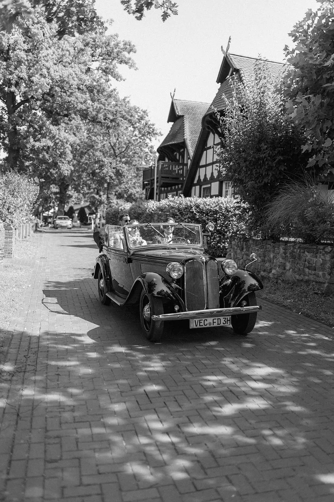 A vintage convertible coming up the lane past a half timbered house
