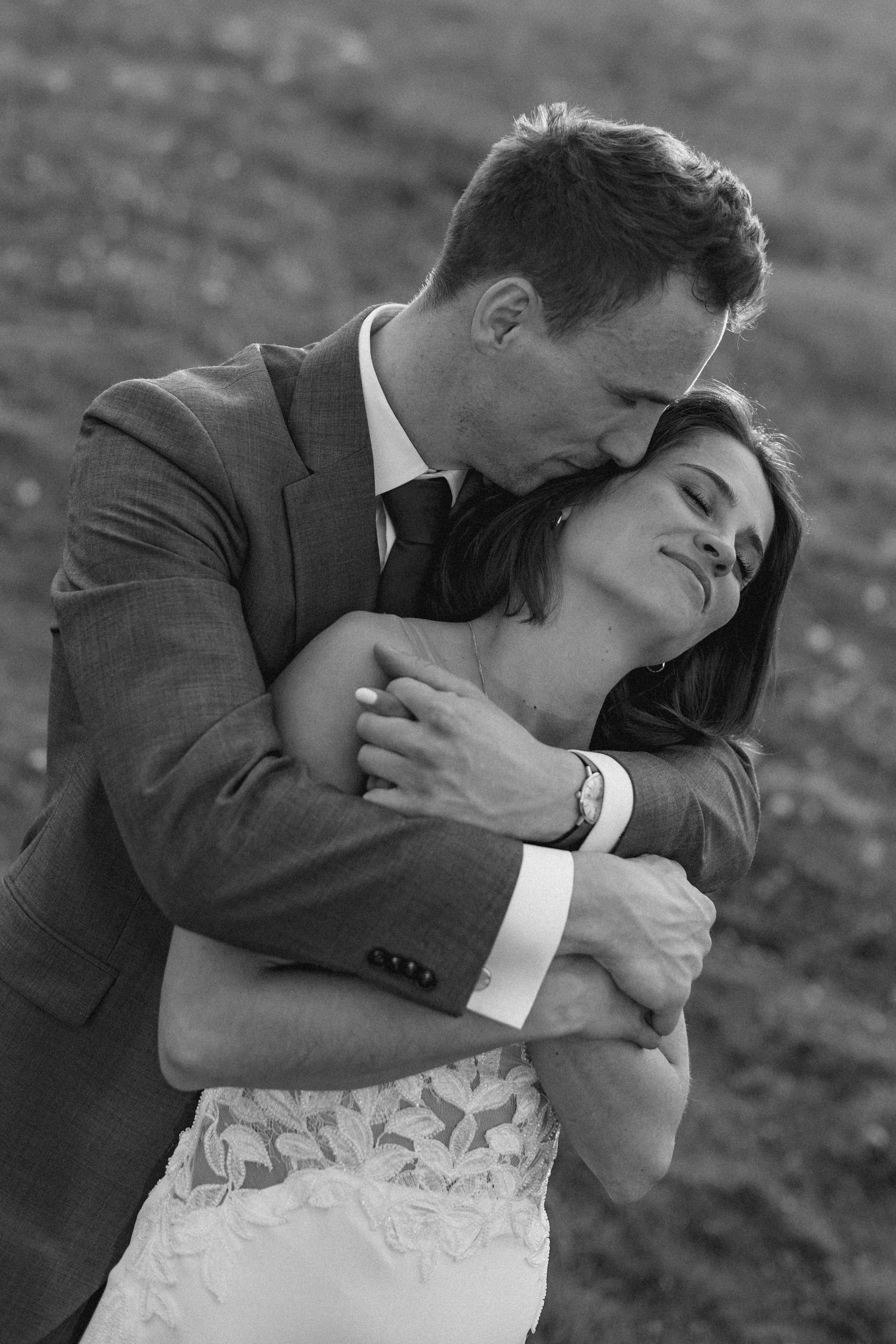 The groom holding the bride from behind, both with eyes closed