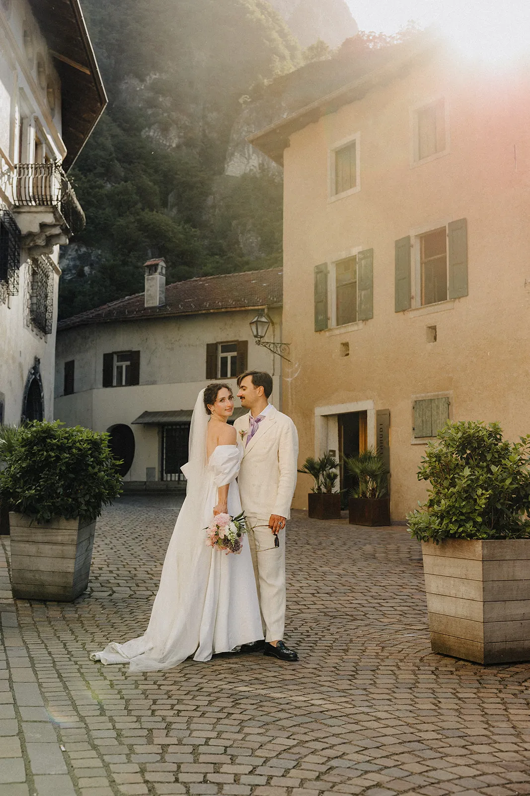The couple kissing in a courtyard, a pale house and hills behind