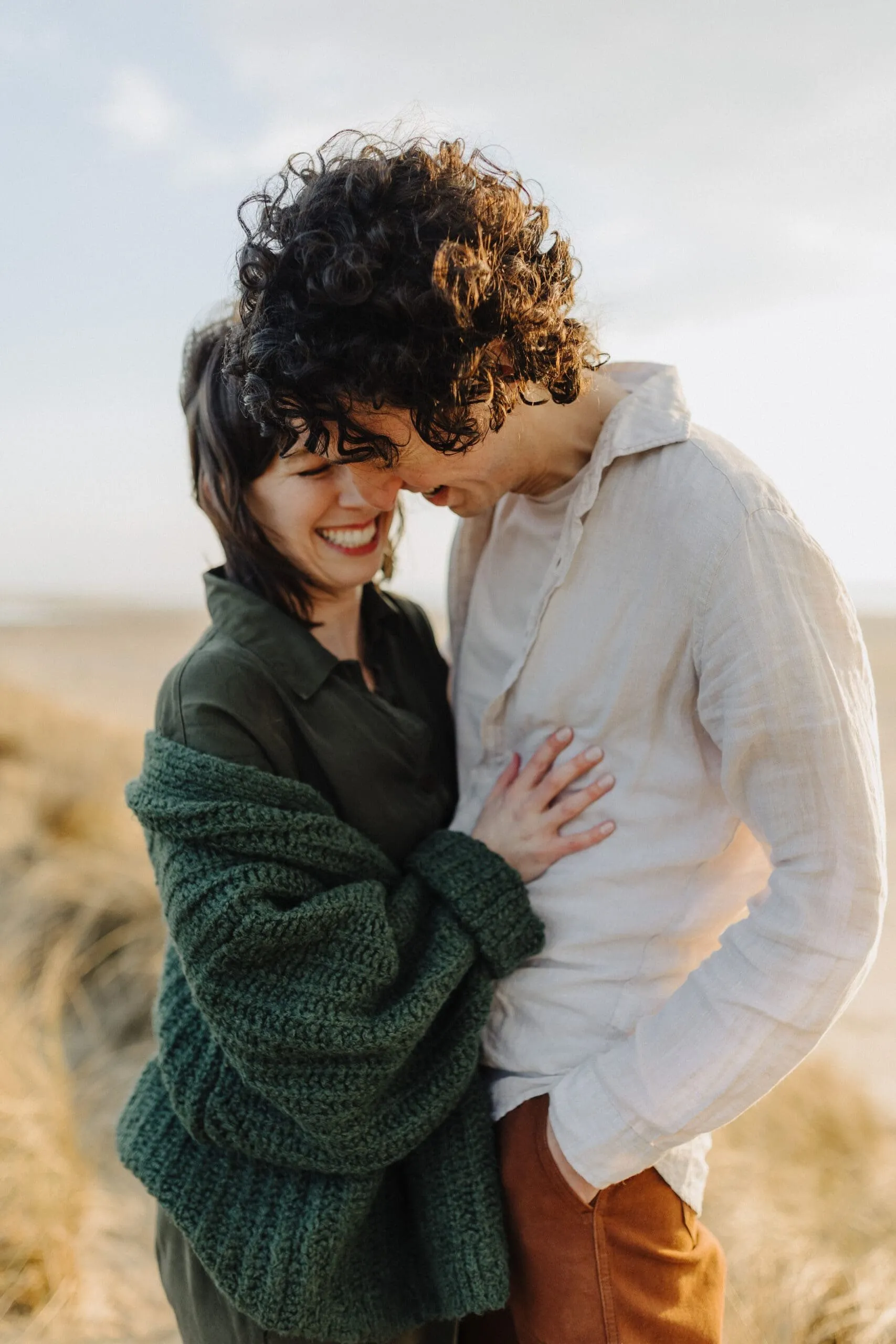 A couple holding each other close in the evening light, his curls blowing in the wind
