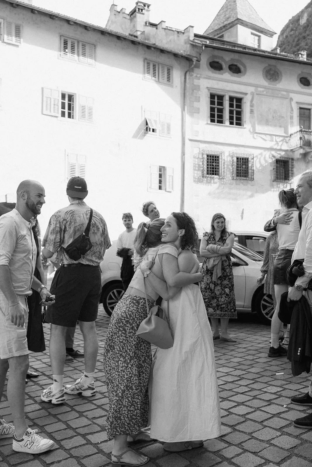 Two guests hugging on the square in front of a frescoed house