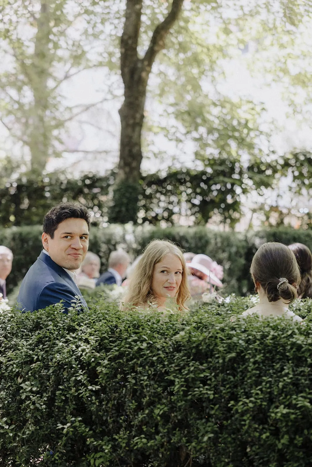 Two guests looking back over the hedge during the ceremony